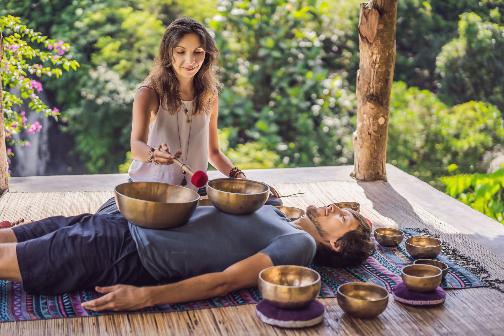 Nepal Buddha copper singing bowl at spa salon. Young beautiful man doing massage therapy singing bowls in the Spa against a waterfall. Sound therapy, recreation, meditation, healthy lifestyle and body care concept